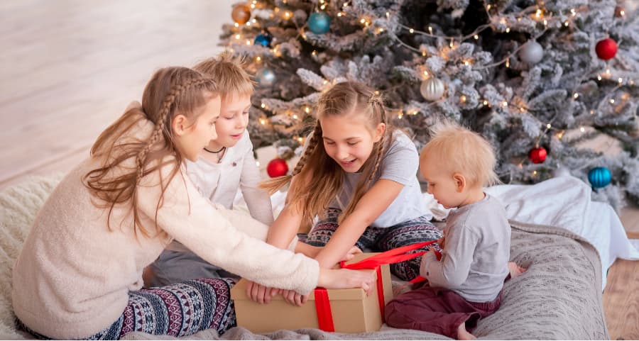 Siblings opening a present in the family room next to a Christmas tree.